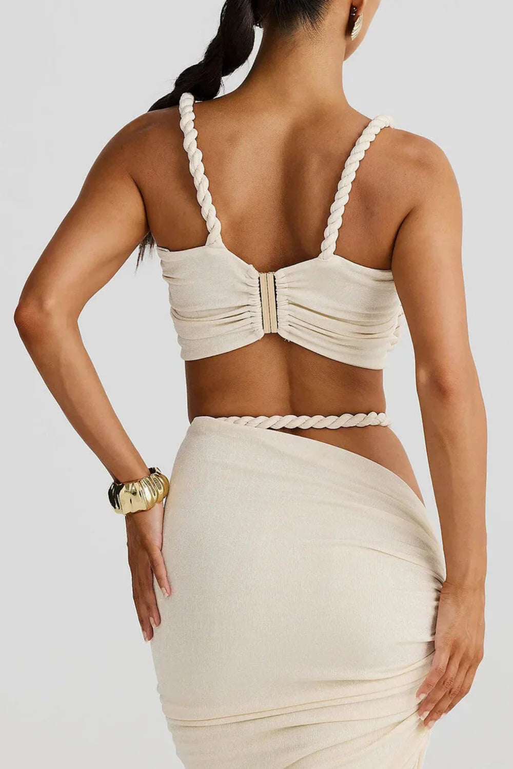 Model wearing Kouvr's The Thelma Set, a beige two-piece Grecian outfit featuring a rope detail bralette top and a ruched asymmetrical maxi skirt