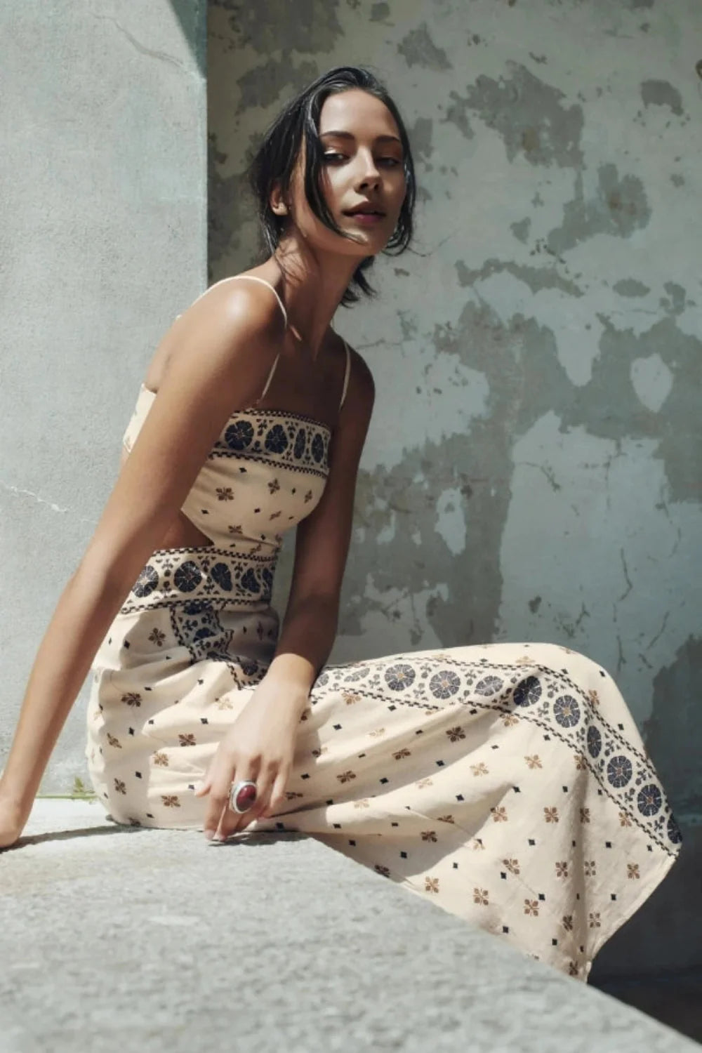 Model wearing Kouvr Vernice embroidered linen cutout midi dress sitting outdoors