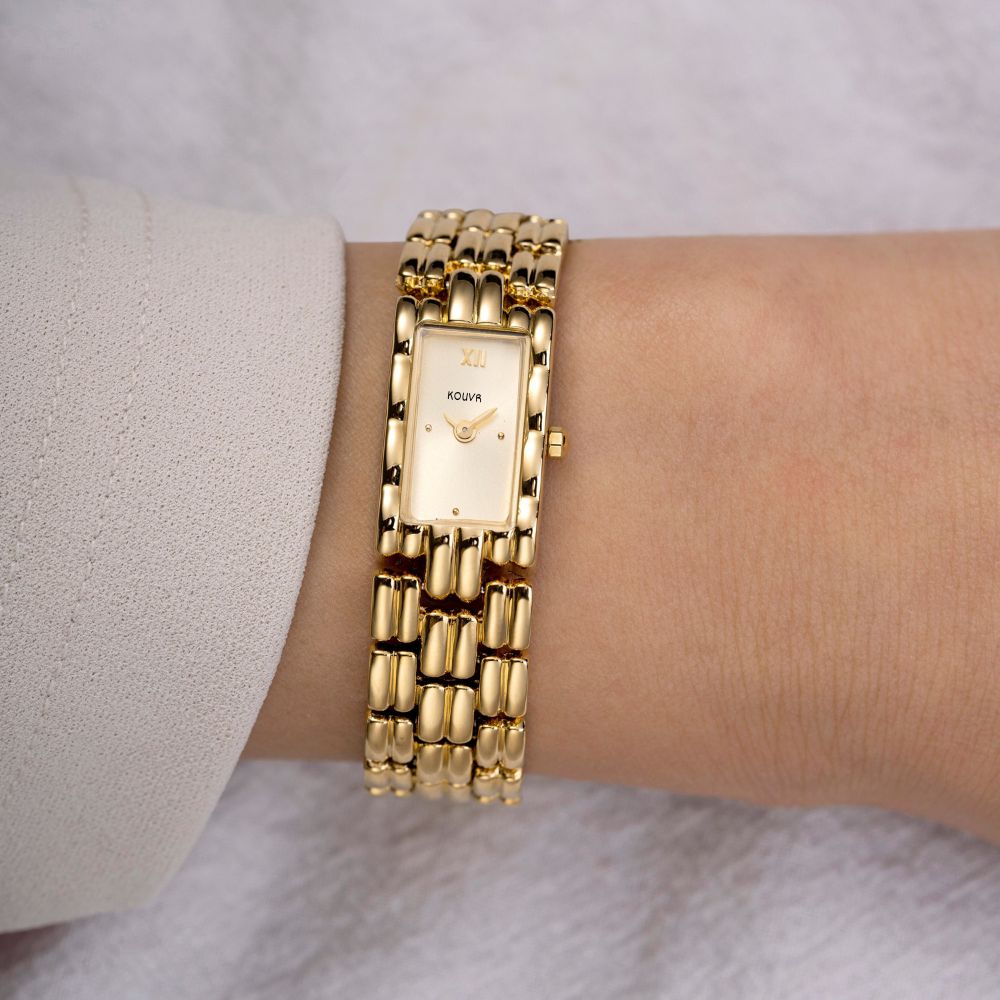 Gold kouvr wristwatch on a wrist with a light background