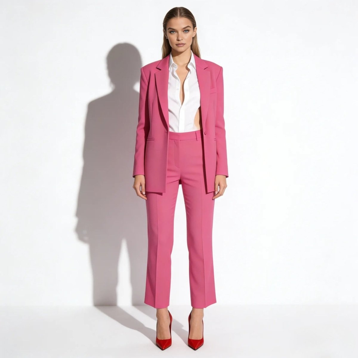 Model wearing the Kouvr hot pink power suit with a white cutout shirt and red stiletto heels against a white background.