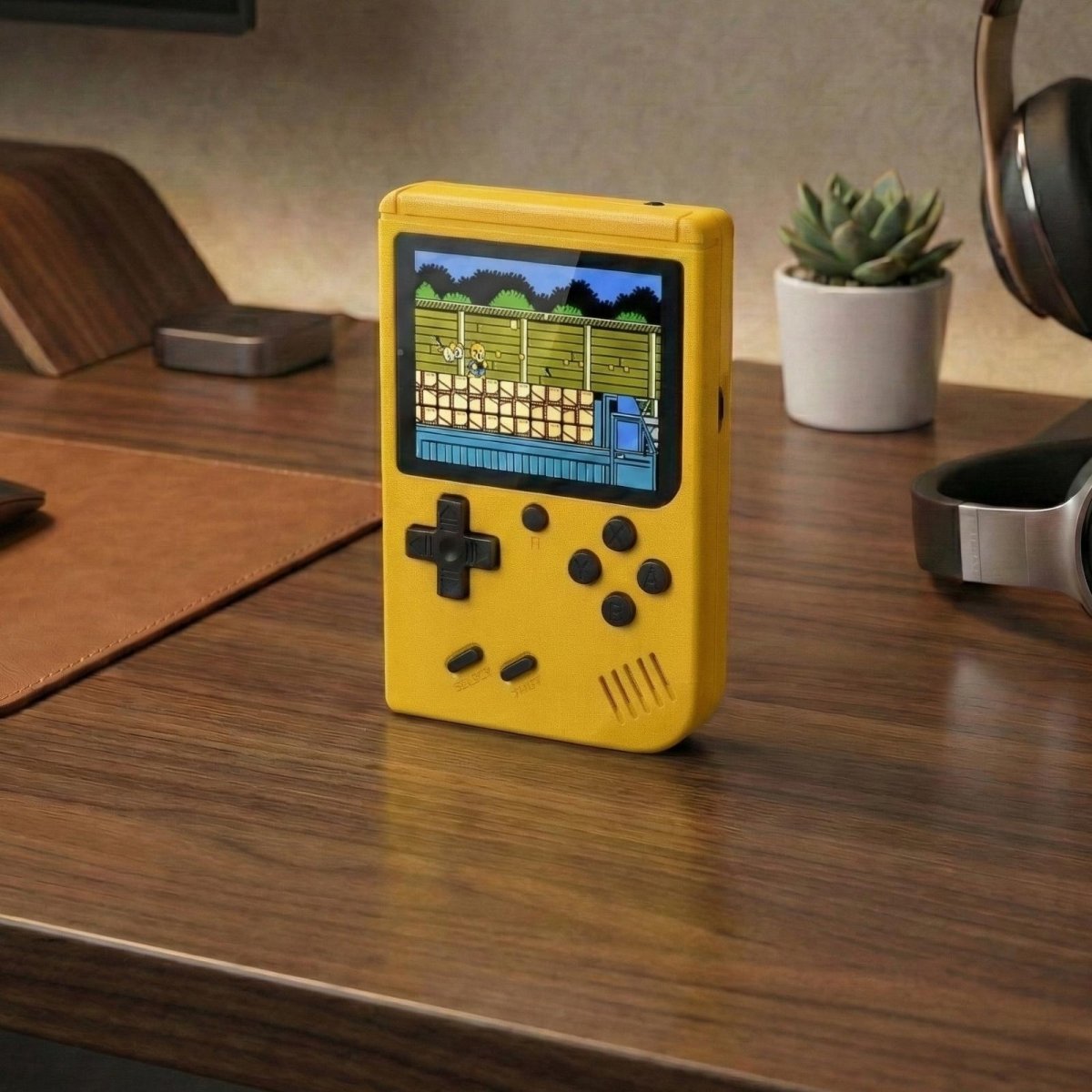 A standalone yellow Kouvr portable classic game console displaying a game on its screen on a modern desk setting.