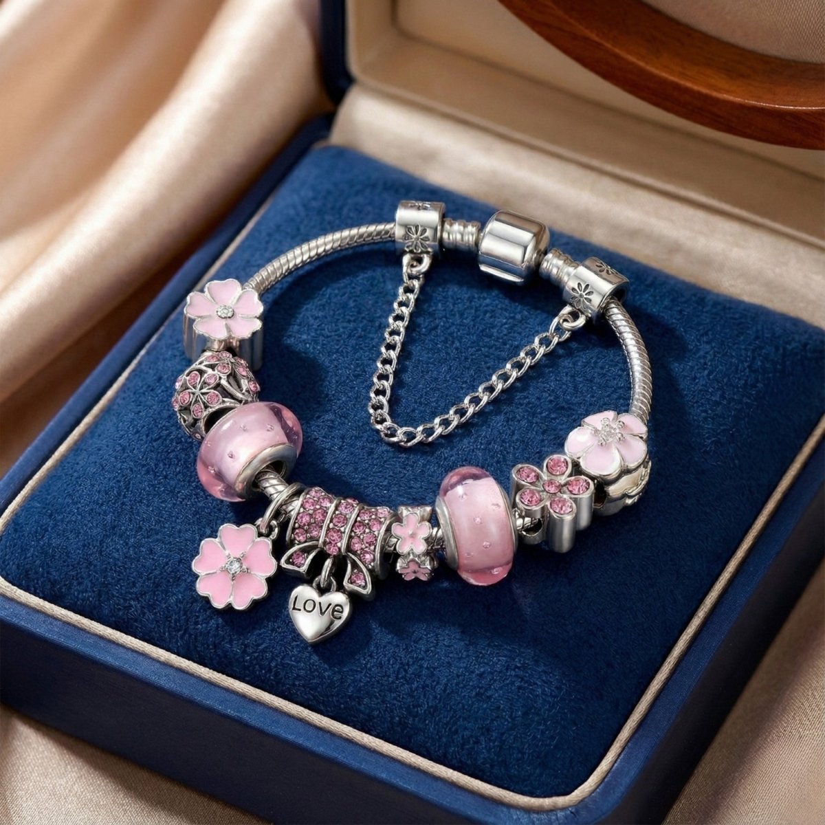 Silver charm bracelet with pink Murano glass beads, pink pave crystal clips, and a "Love" heart pendant resting inside a blue jewelry box.