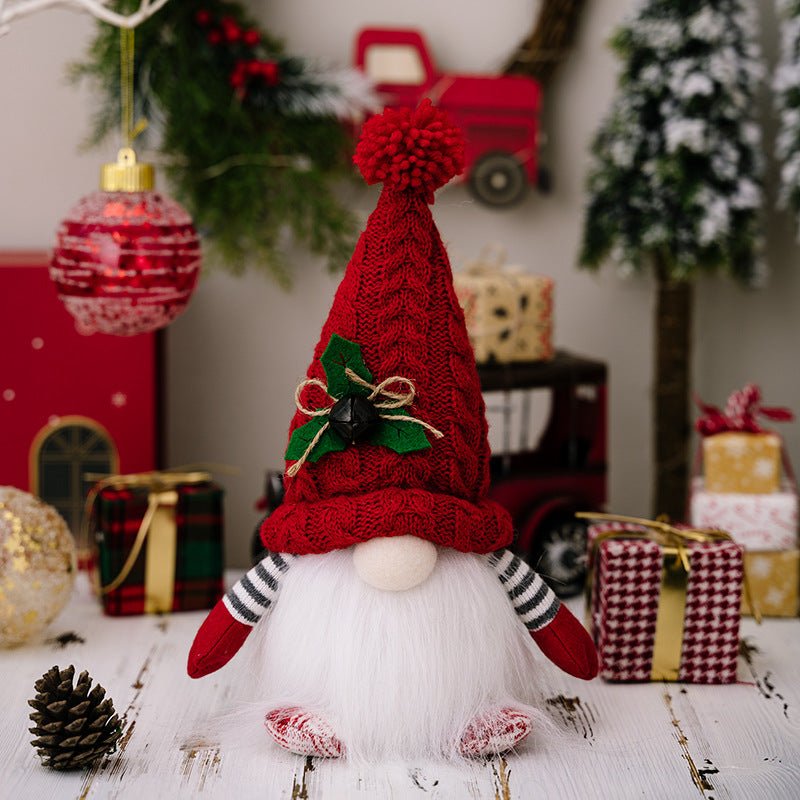A single red Christmas gnome with a textured knit hat adorned with a bell and holly, featuring a full white beard, sitting among holiday decorations.