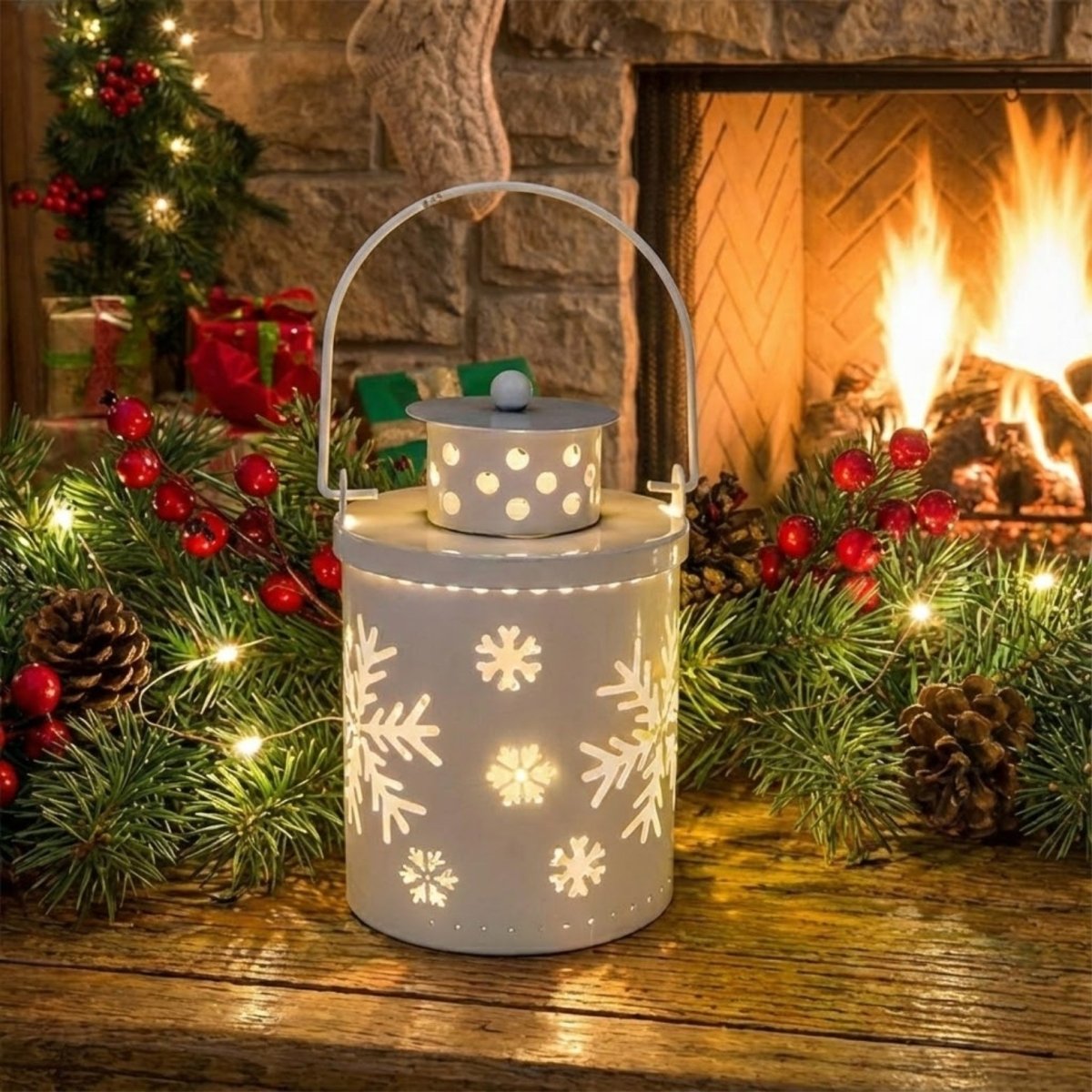 White metal cylinder lantern with cutout snowflake designs glowing warmly, sitting on a rustic wooden mantel surrounded by pine garland and red berries.