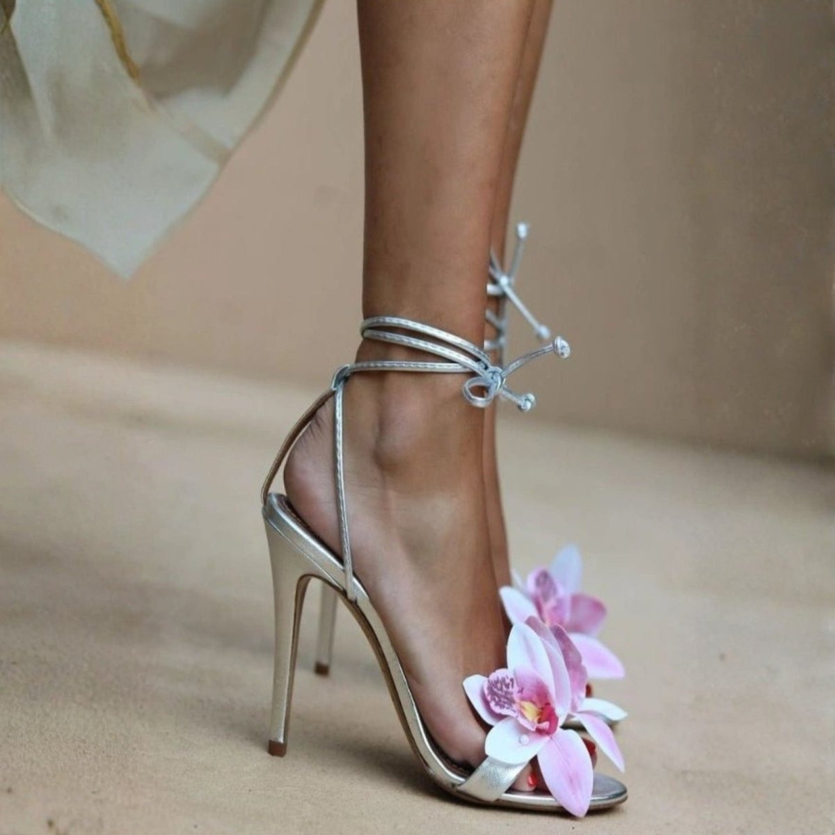 Silver high-heeled sandal with pink flowers on a neutral background