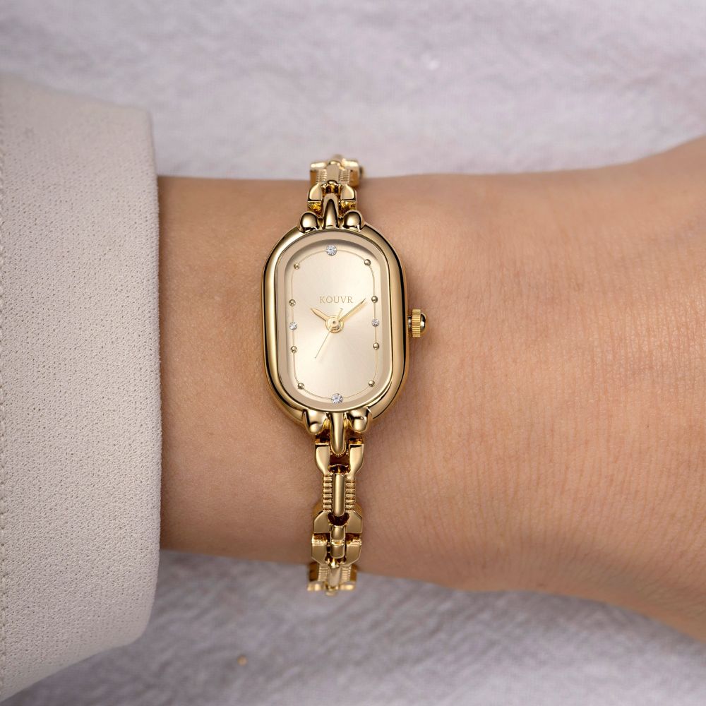 Gold Kouvr wristwatch on a wrist with a neutral background