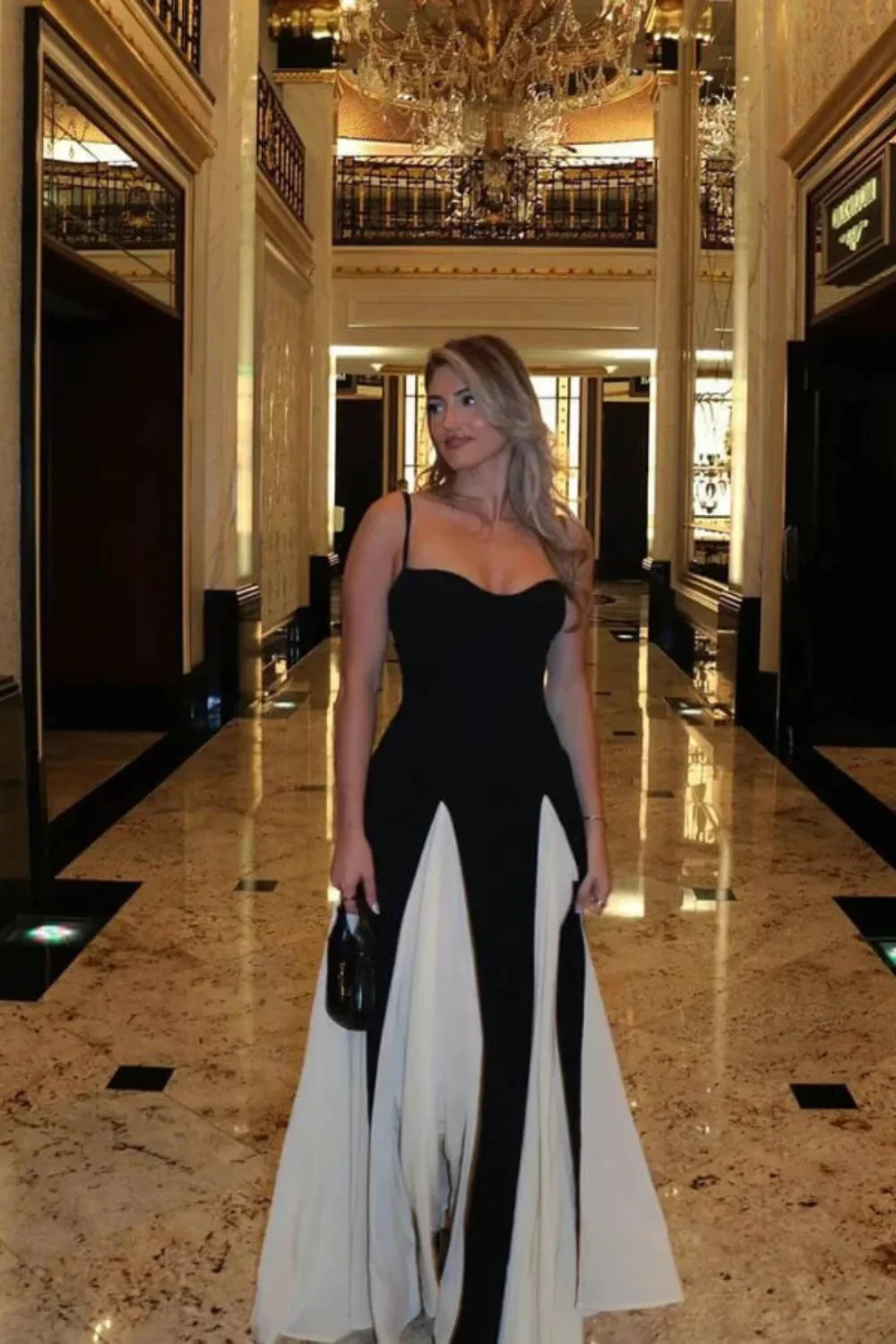 Woman wearing the Kouvr Anastasia black formal gown standing on an elegant marble hallway