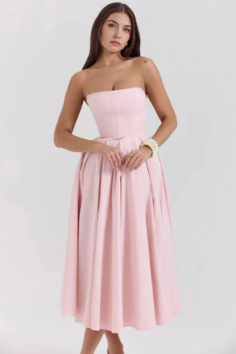 Model wearing the Kouvr Fashion blush pink strapless midi dress with a full pleated skirt