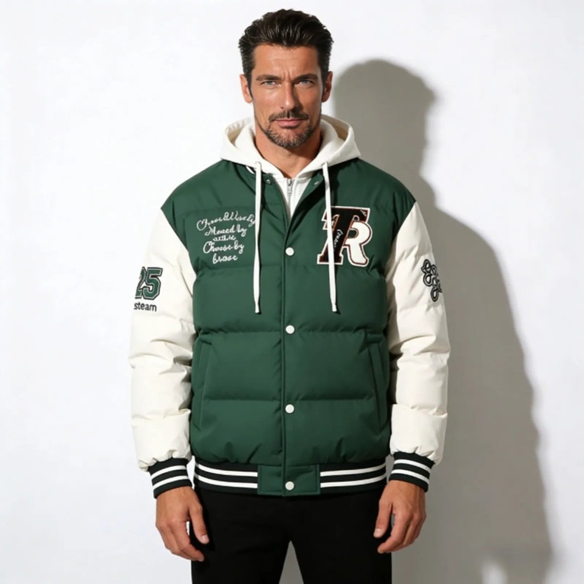 Man wearing the Kouvr Angelo Hooded Puffer Varsity Jacket in green, showing the embroidered front 'R' patch and script detailing.