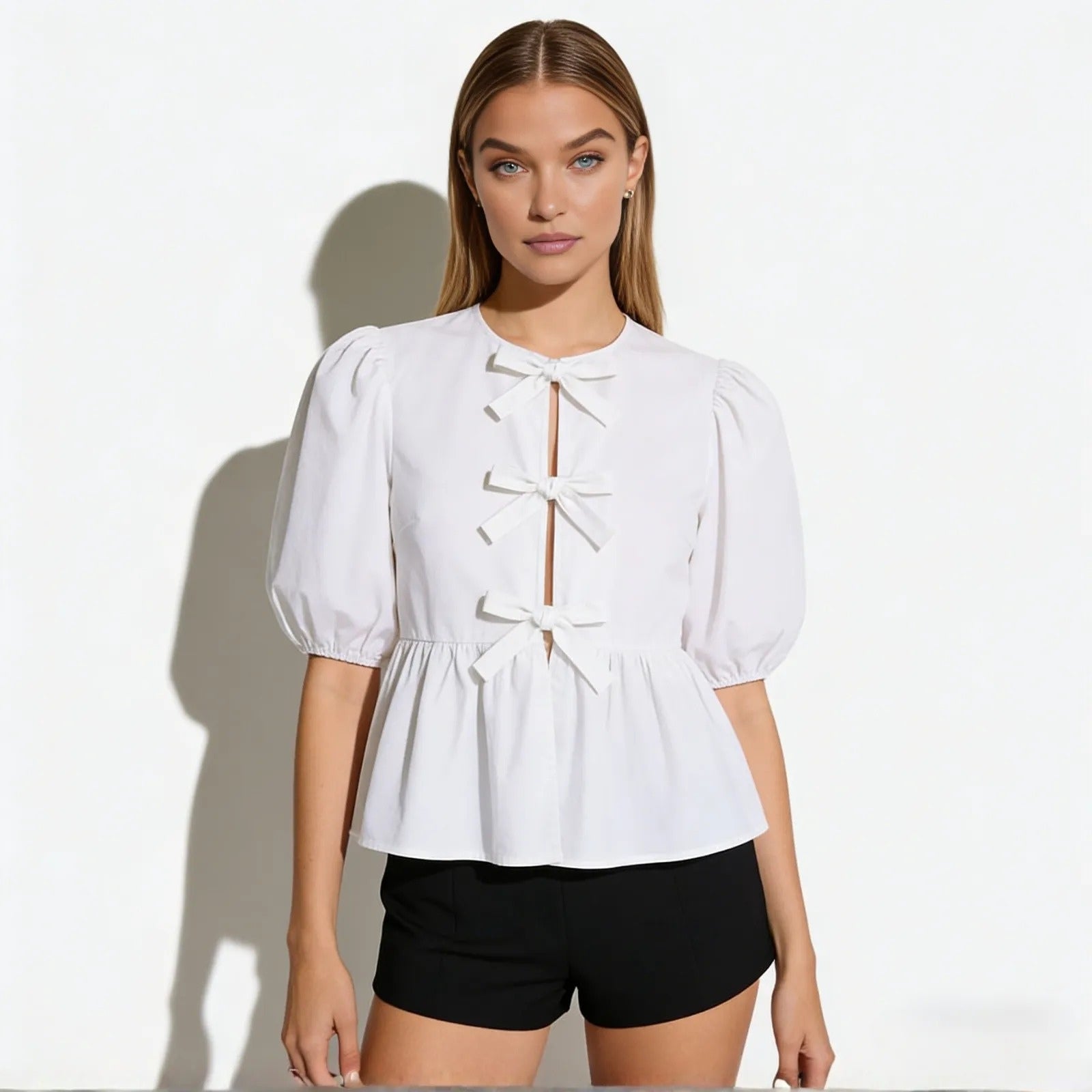 Model wearing the Kouvr Anne white cotton poplin blouse with puff sleeves and three front bows, paired with black shorts.