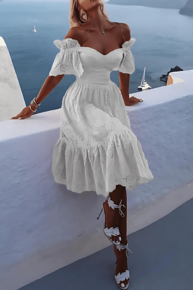 Model wearing the Kouvr Annie white eyelet midi dress on a balcony overlooking the ocean