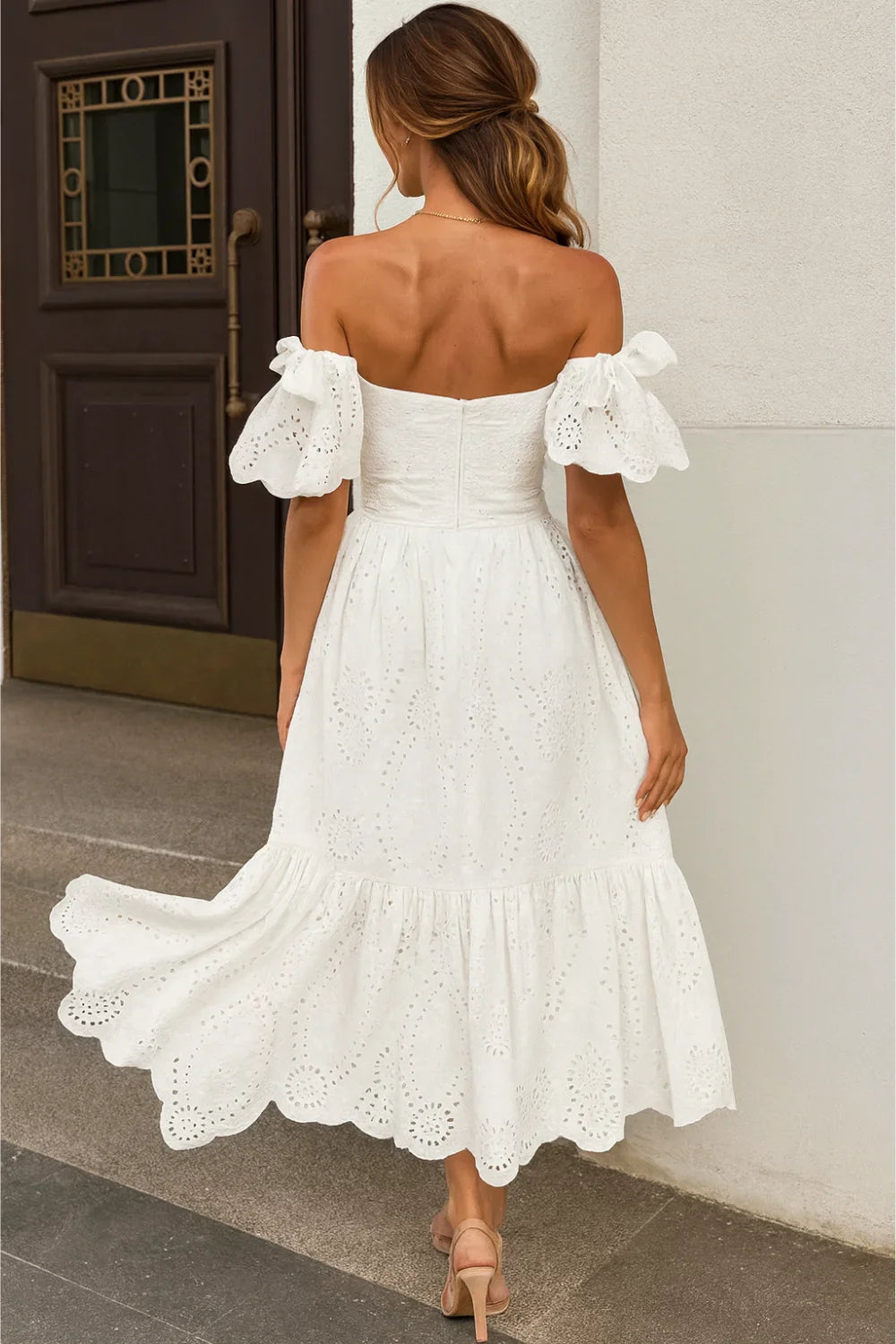 Model wearing the Kouvr Annie white eyelet midi dress on a balcony overlooking the ocean