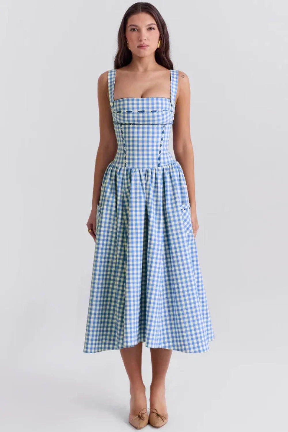 Model wearing the Kouvr Apolline blue gingham midi dress with a structured corset bodice and square neckline, standing in a garden