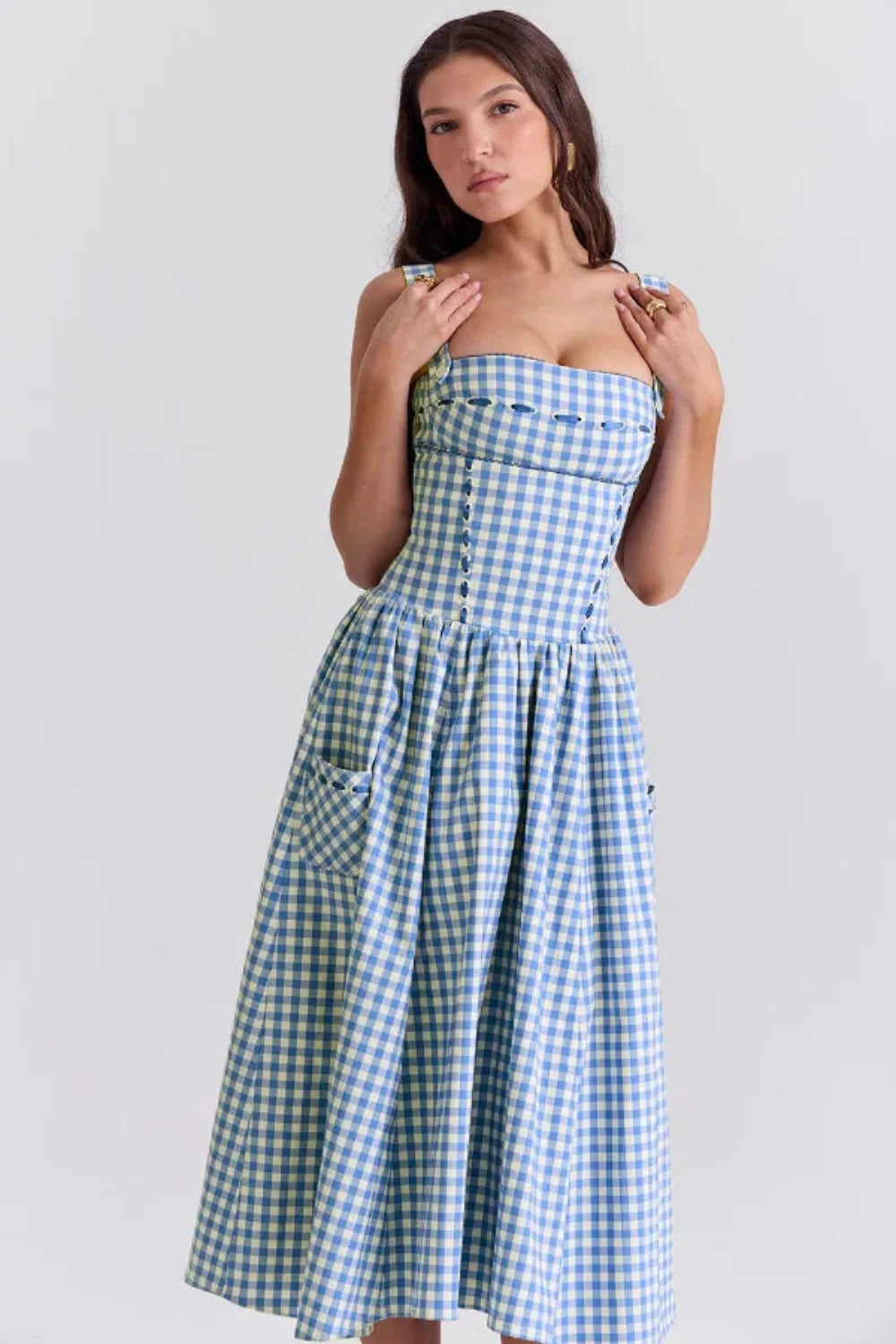 Model wearing the Kouvr Apolline blue gingham midi dress with a structured corset bodice and square neckline, standing in a garden