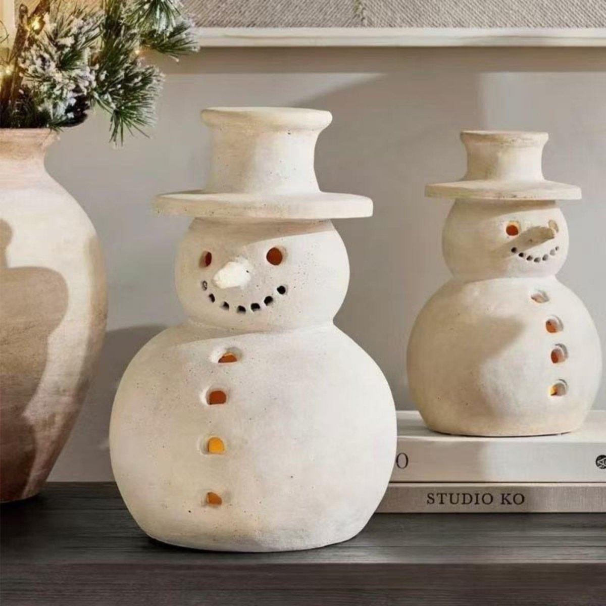 Close-up detail of two artisan ceramic snowman luminaries on a shelf, highlighting the textured matte finish and hand-carved features.
