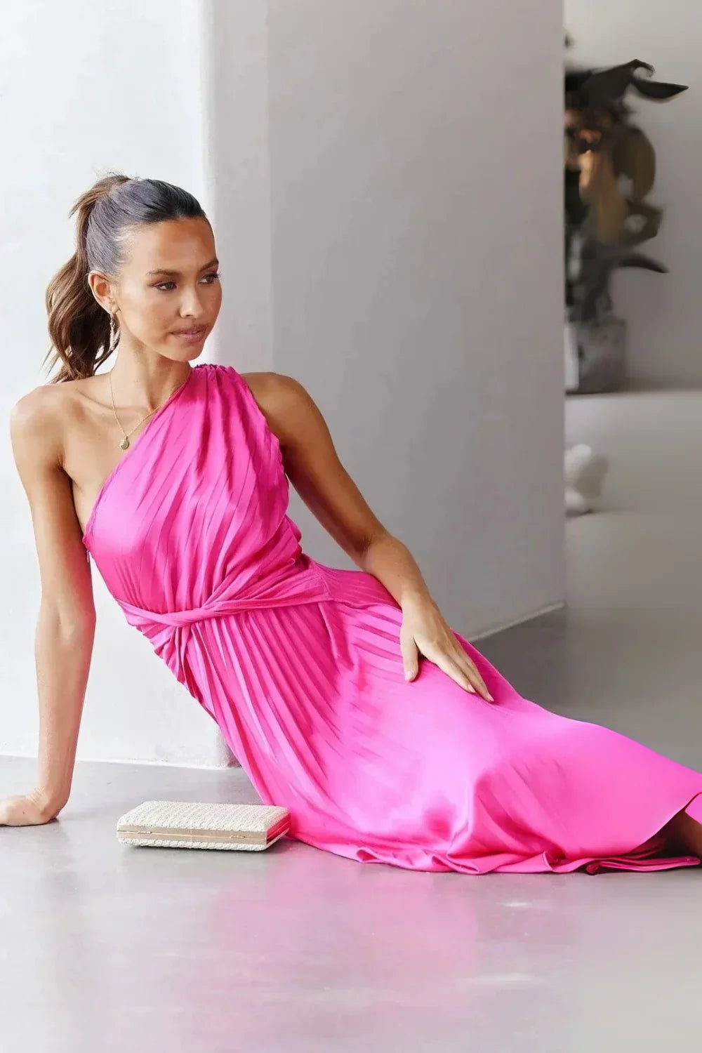 Woman wearing Kouvr Fashion hot pink one shoulder pleated dress with a white clutch' and 'Detail shot of the twist knot waist on a satin pink cocktail dress