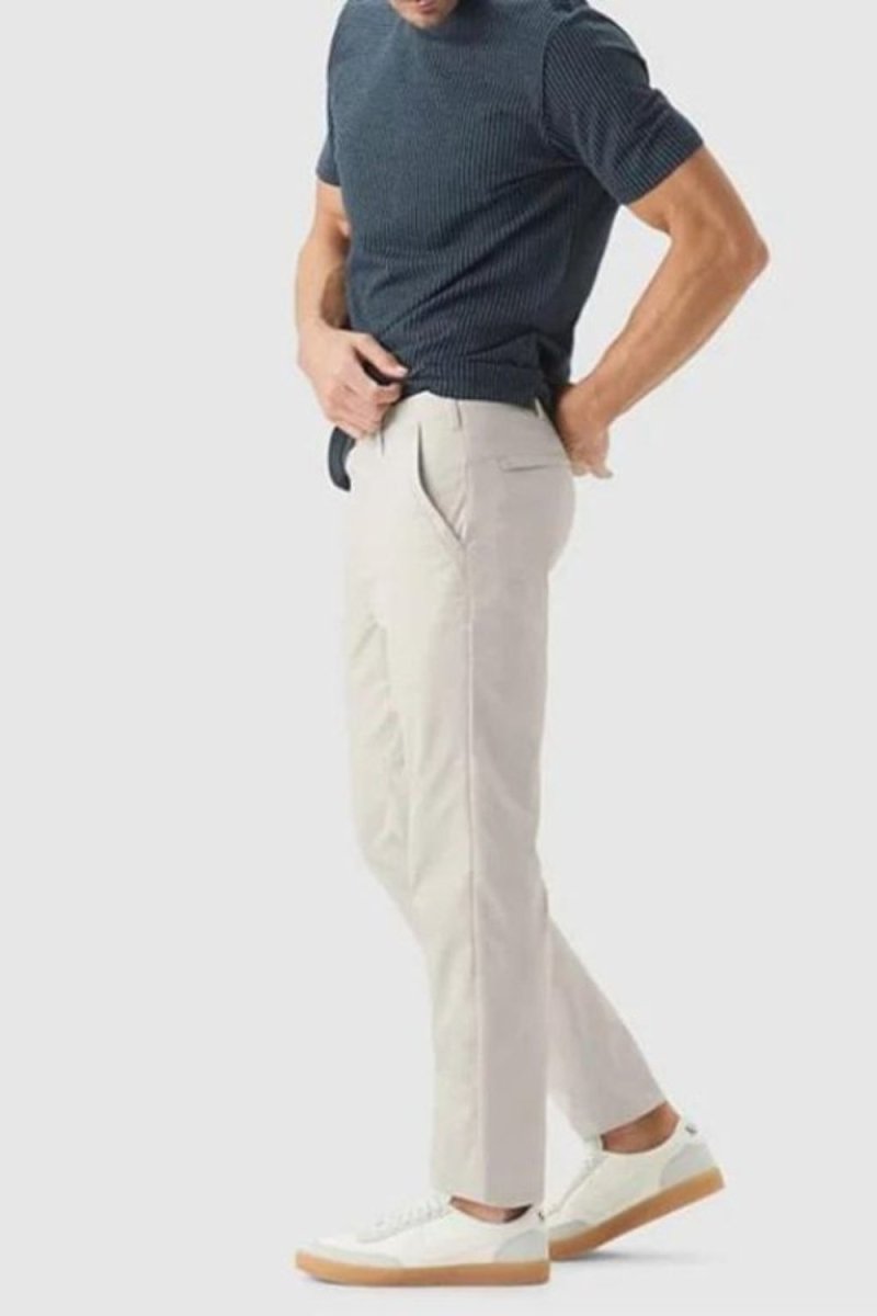 Man wearing Kouvr slim fit tech chinos in stone white with a dark navy t-shirt and white leather sneakers