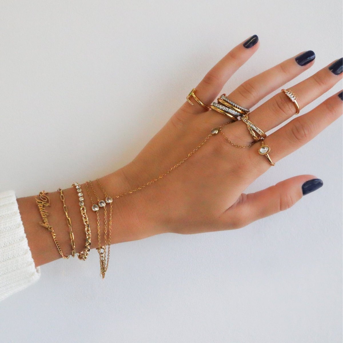Kouvr wearing multiple gold rings and bracelets on a white background