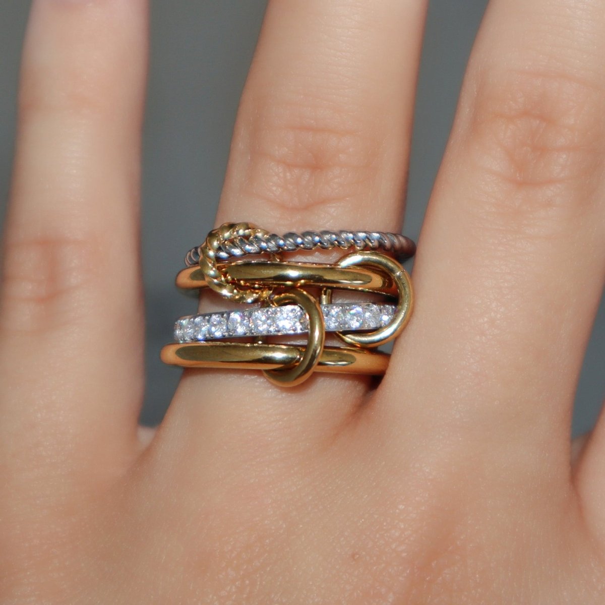 Gold and silver kouvr ring with diamond accents on a finger against a neutral background