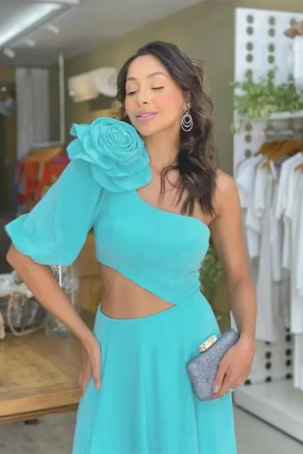 Model standing on a staircase wearing the Kouvr light blue one-shoulder dress with a large flower detail and side cutout