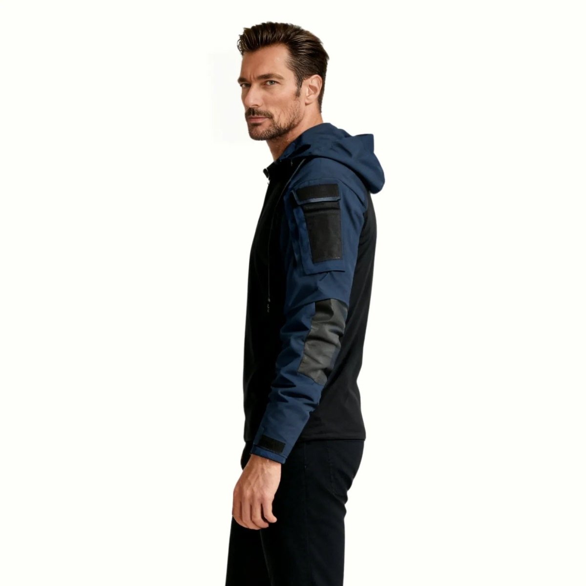 Side profile of a man wearing the Kouvr Ares techwear hoodie, highlighting the shoulder pocket, loop field, and reinforced elbow patch.
