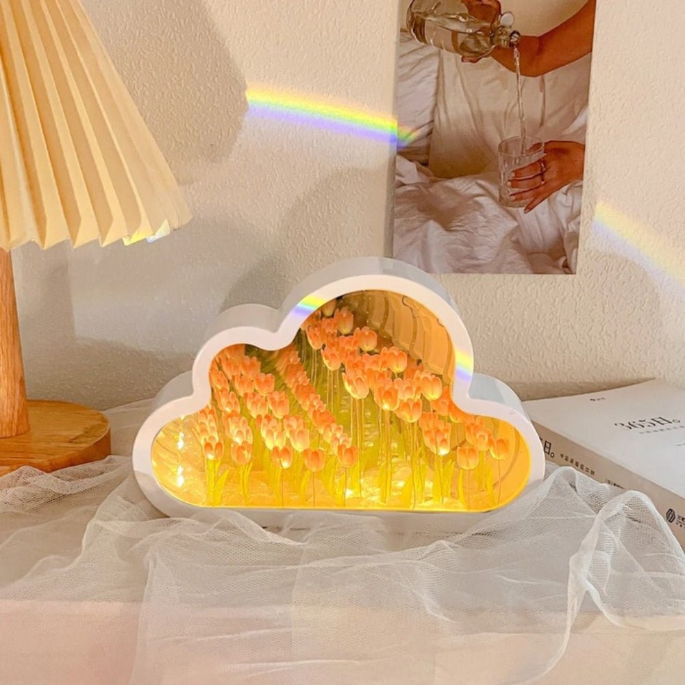 Kouvr Cloud Tulip Infinity Mirror Lamp in Sunset Peach, casting a warm ambient glow on a bedside table with a rainbow light flare.
