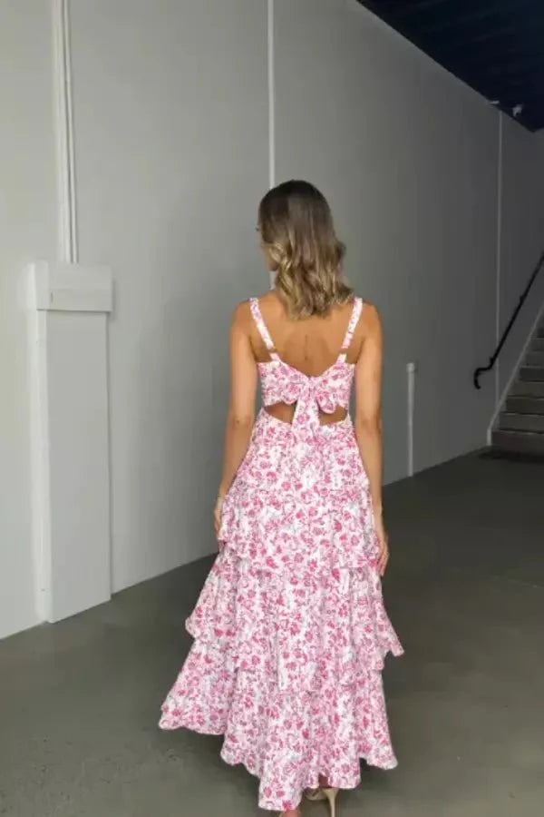 Model wearing the Kouvr Denise pink floral tiered midi dress with a square neckline and open-back bow detail at a garden party