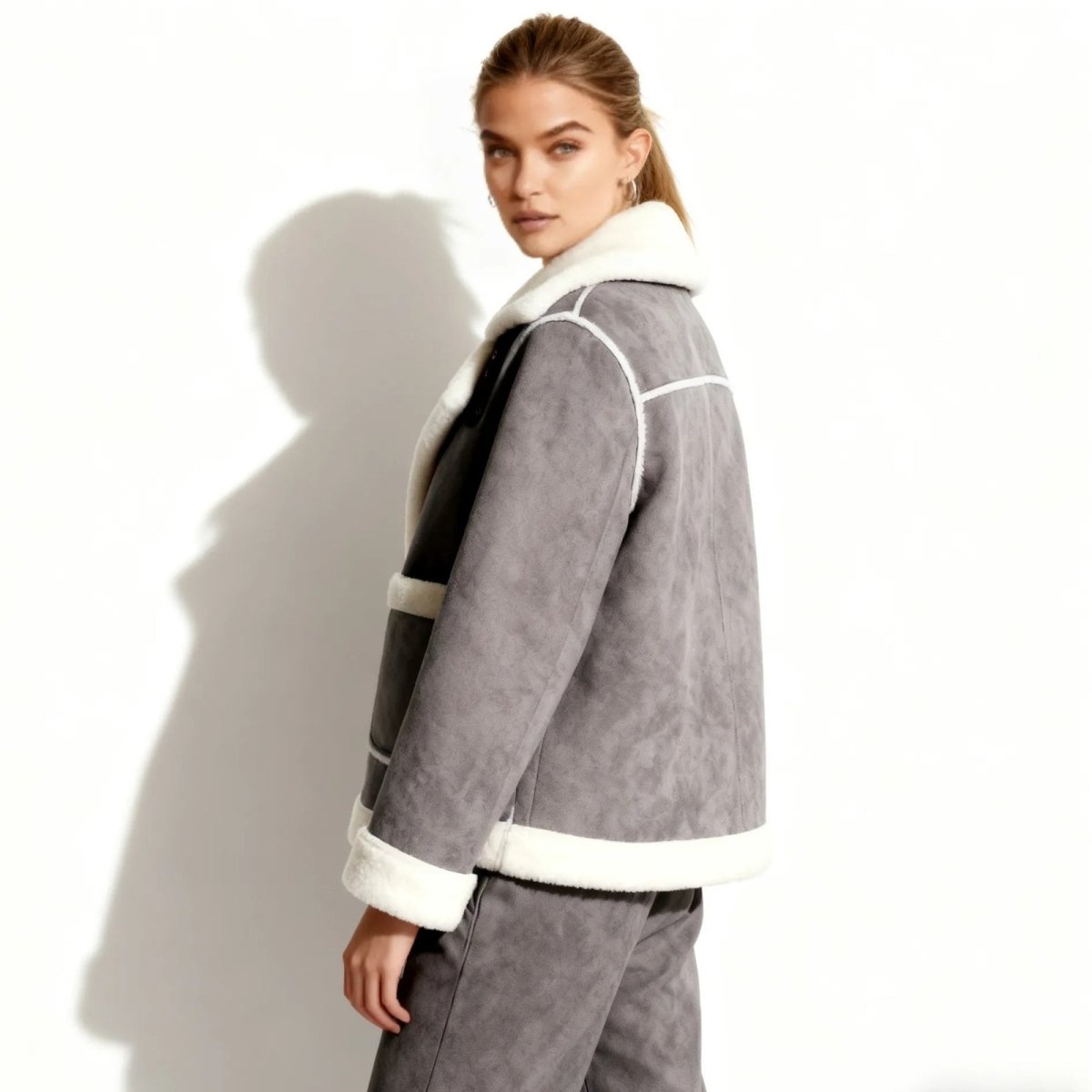Model looking over her shoulder to show the side profile and fit of the Kouvr Esmeralda grey faux suede shearling jacket.