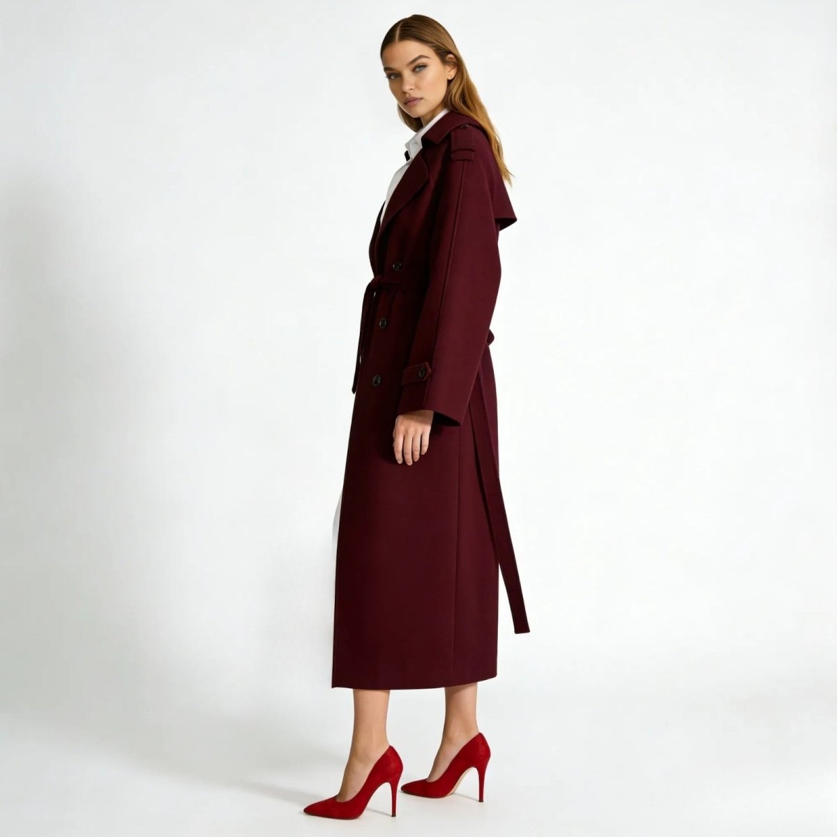 Side view of a model in the Kouvr Fashion Esther burgundy wool trench coat, showcasing its long silhouette, sleeve details, and graceful drape.