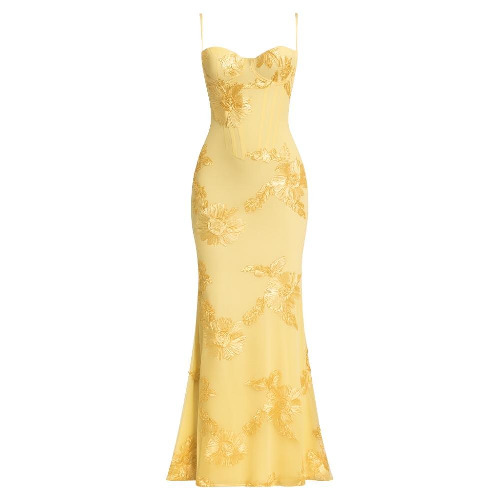 A model viewed from the back wearing the Kouvr Fashion Aphaea Gown, a backless yellow mermaid dress with 3D floral embroidery and an adjustable lace-up corset detail