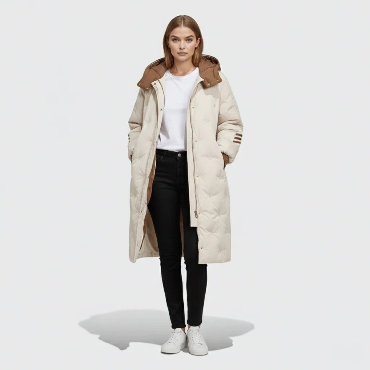Model wearing the Kouvr Fashion Arianne long quilted down puffer coat in ivory with a contrasting brown hood, styled with black jeans and white sneakers.