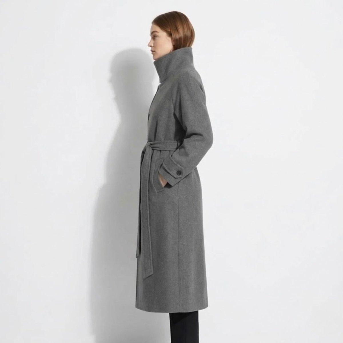 Side profile of a model in the heather grey Ashley wool coat, highlighting the high funnel neck design, full length, and elegant drape.