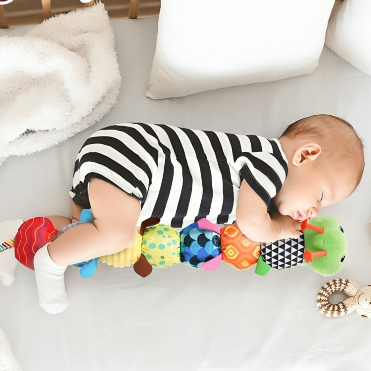 Baby in a striped outfit playing with colorful toys on a light surface.