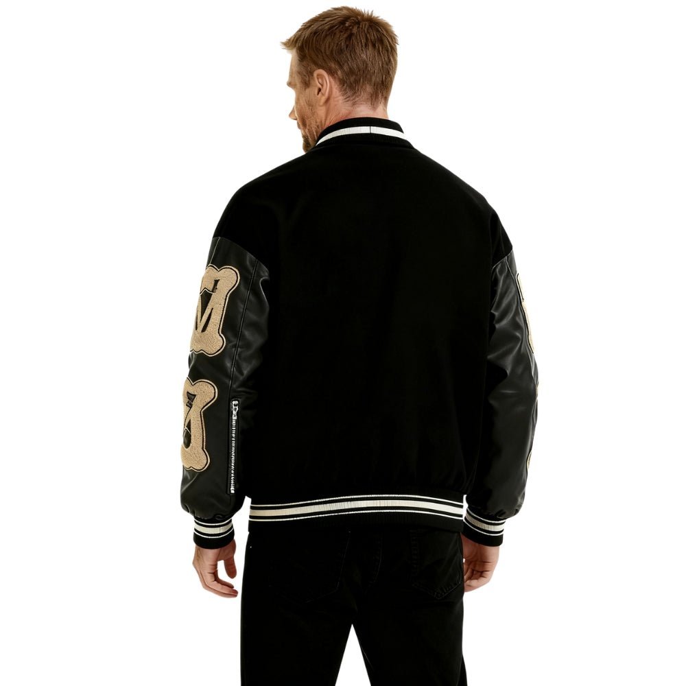 Person wearing a black Kouvr jacket with gold designs on the back, standing against a white background
