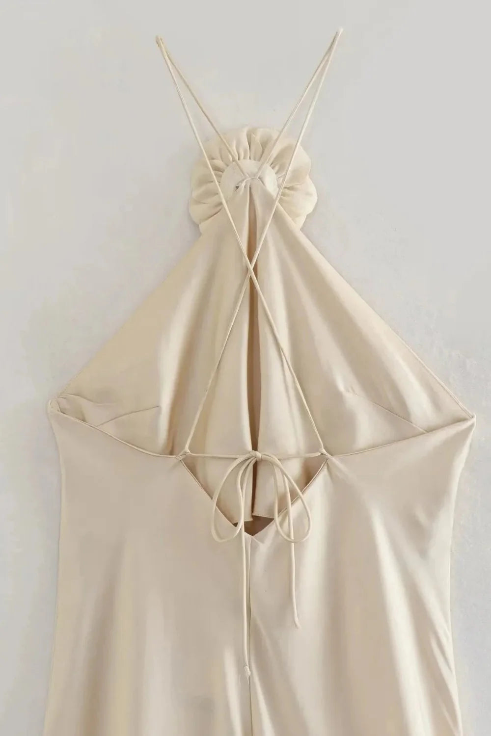 Model from behind wearing the Kouvr Fashion Cathalina beige satin halter dress showing the open back and criss-cross straps