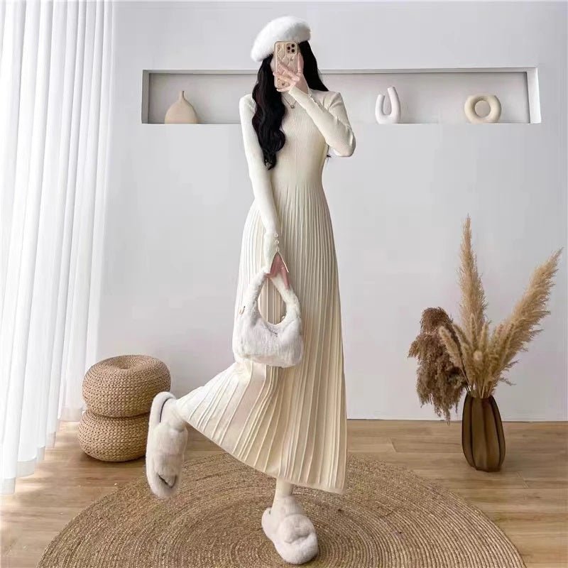 Model playfully kicking one leg up to show the fluid movement of the ivory pleated knit dress by Kouvr Fashion.