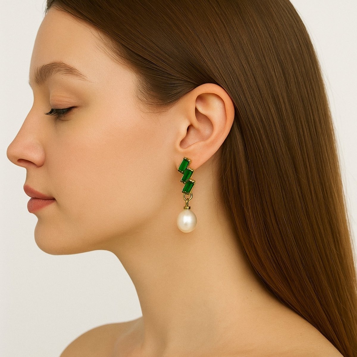 Close-up of a woman wearing green geometric Kouvr earrings with a pearl drop on a neutral background