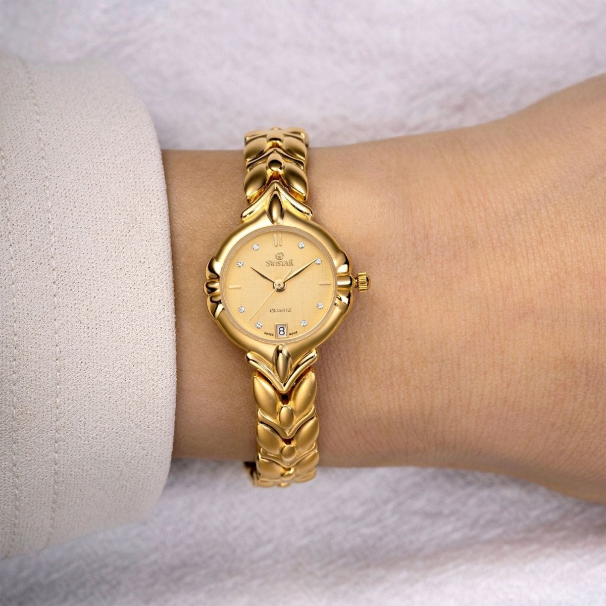 A woman wearing the Kouvr Fashion Evanthe gold leaf bracelet watch with a champagne dial.