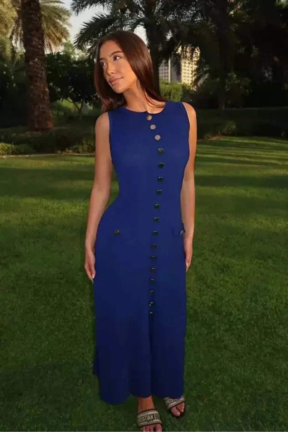A woman wearing the Kouvr Fashion Fiorella blue sleeveless button-front midi dress in an elegant garden setting