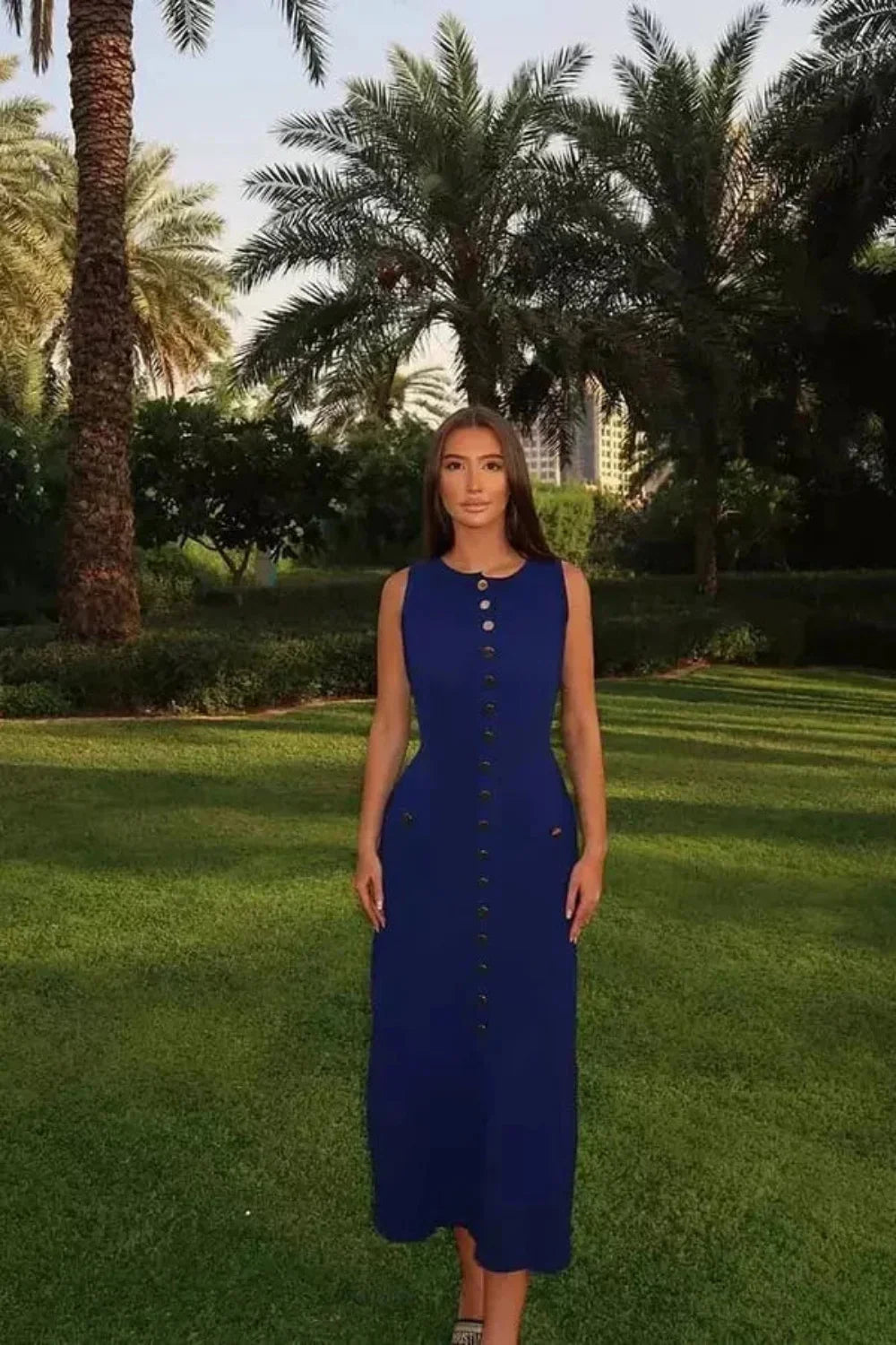 A woman wearing the Kouvr Fashion Fiorella blue sleeveless button-front midi dress in an elegant garden setting
