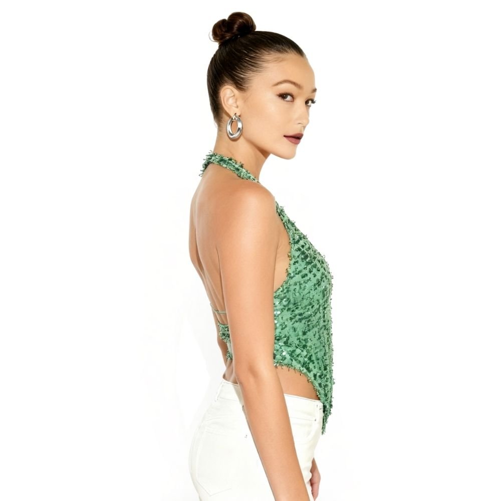 Woman wearing a kouvr  green textured top with white pants on a white background