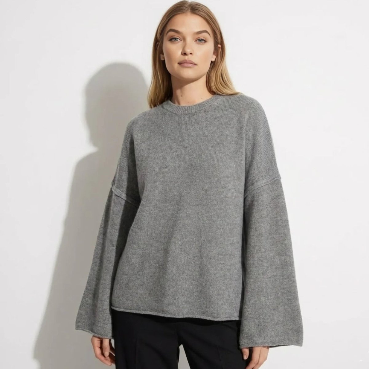 Model wearing the Kouvr Fashion grey oversized bell sleeve sweater made from a cashmere and merino wool blend.