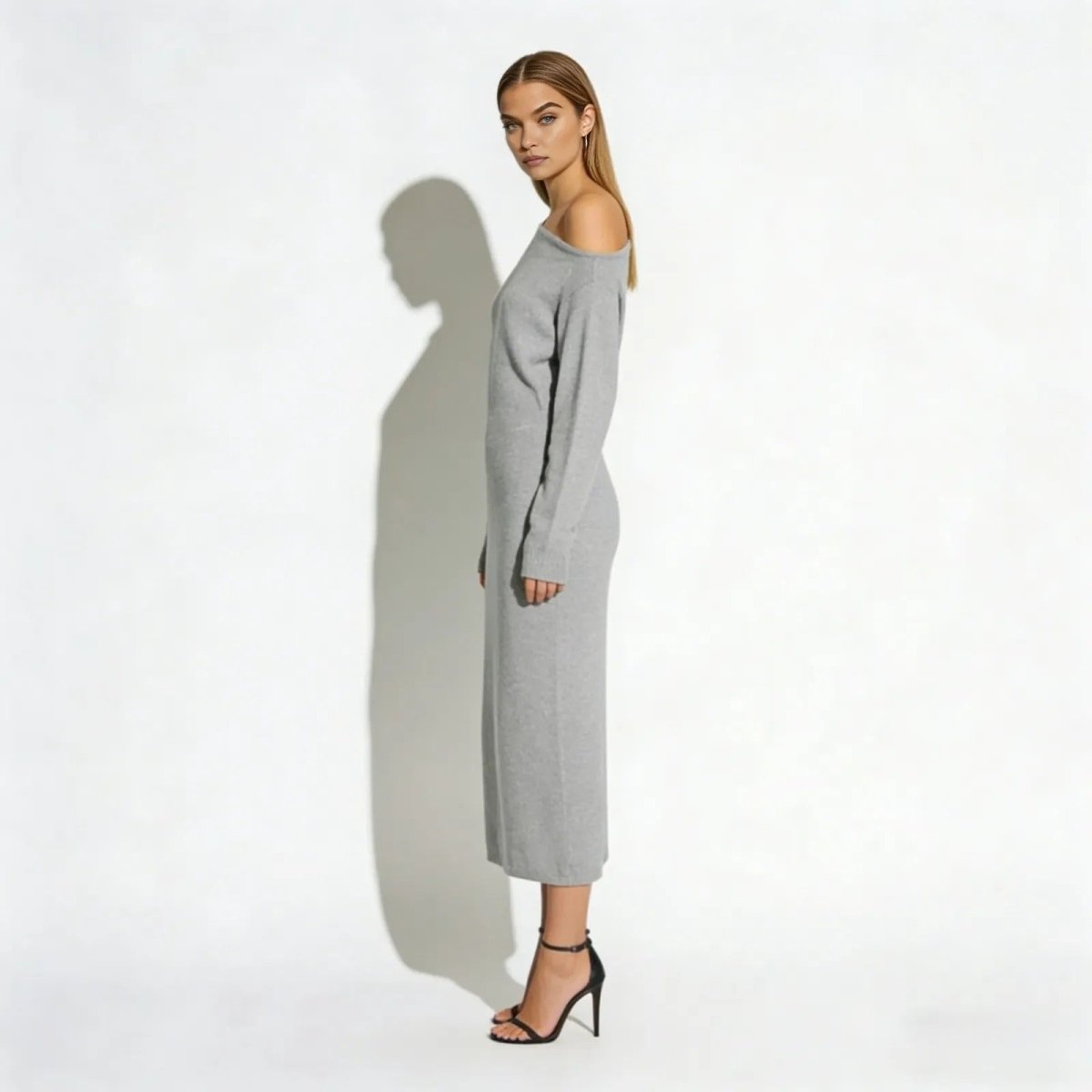 Side profile of a model in a light grey long sleeve asymmetrical sweater dress with black heels.
