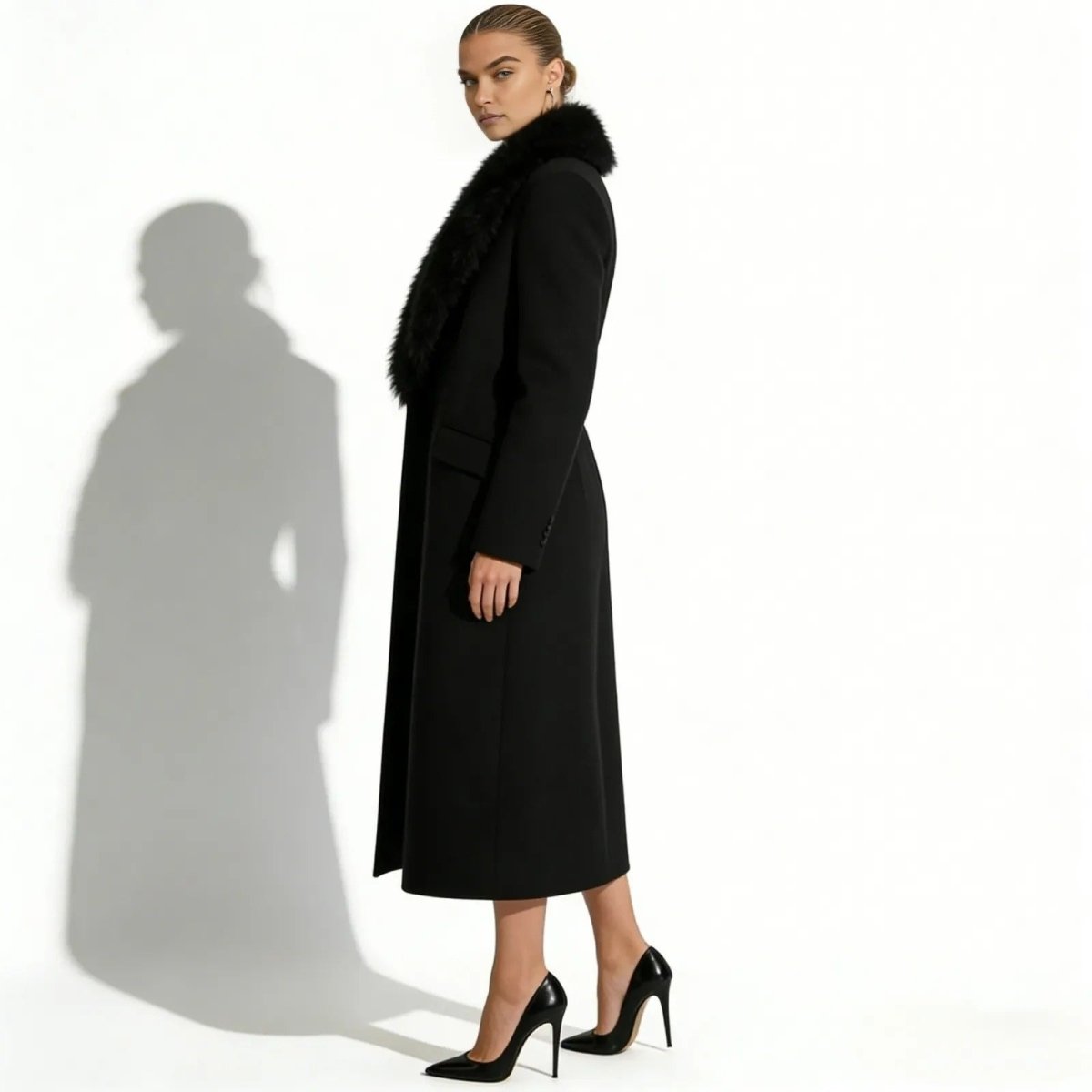 Model from the side wearing the Kouvr Fashion long black single-breasted wool coat with a plush black faux fur collar and black stiletto heels.