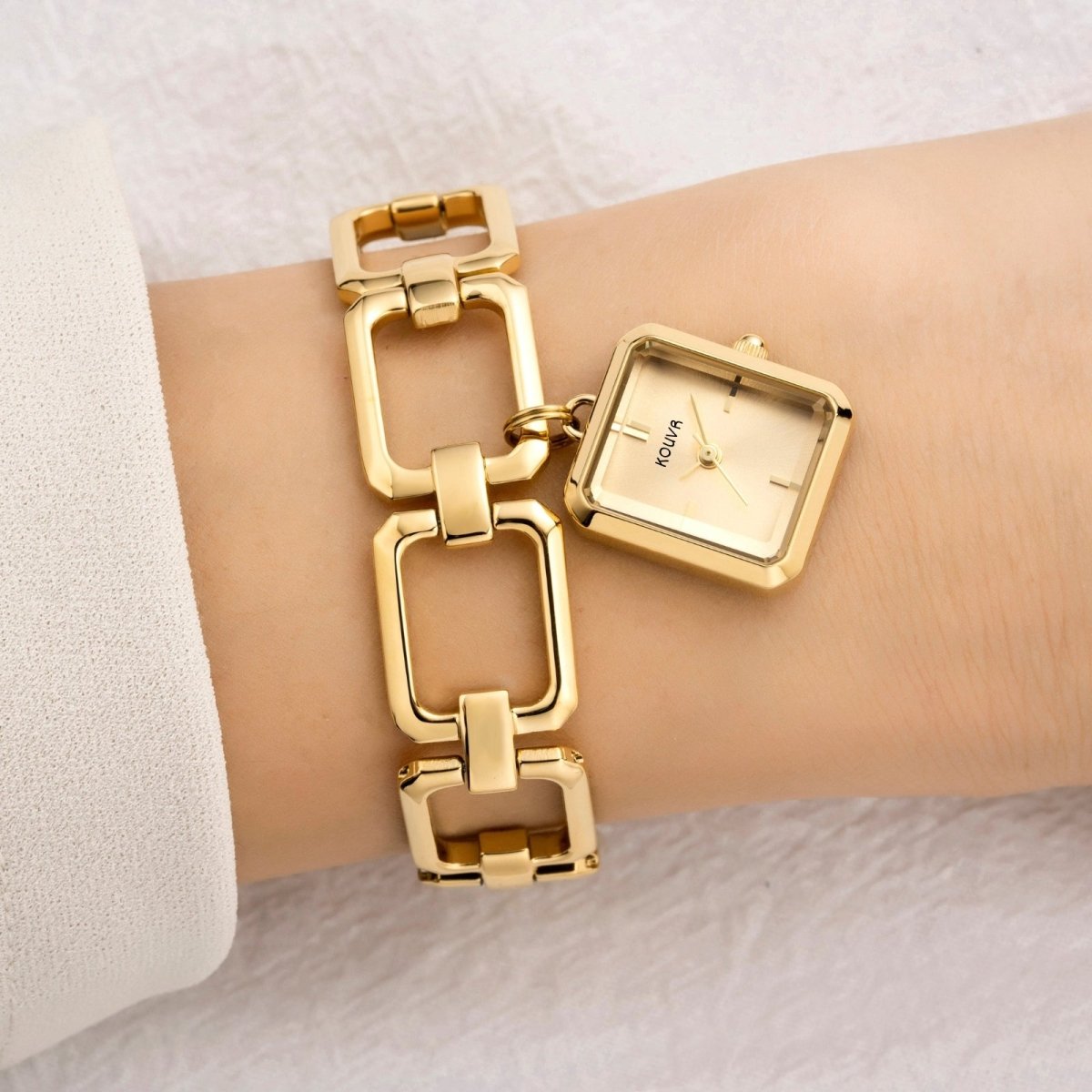 Gold kouvr watch and bracelet set on a wrist against a white background