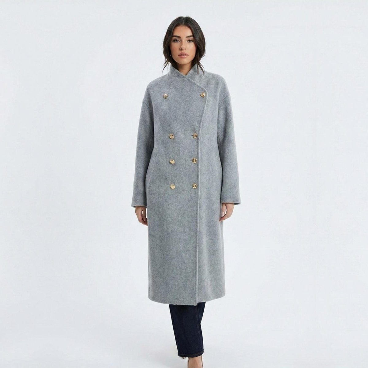 Madison Beer wearing the Maddie long grey double-breasted wool coat from Kouvr Fashion, buttoned to the top with a funnel neck, against a white background.