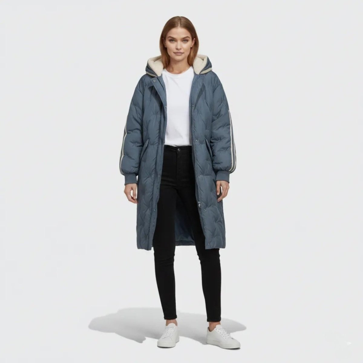 Woman wearing the Kouvr Fashion Meridian long quilted down parka in slate dark blue with a sherpa-lined hood, front view.
