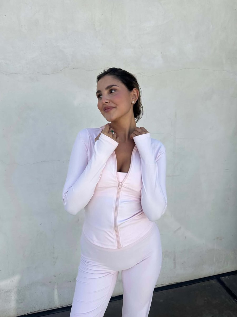Woman smiling in a light pink Kouvr Fashion Nola Sculpt Jacket and matching leggings, demonstrating the complete athleisure set outdoors.