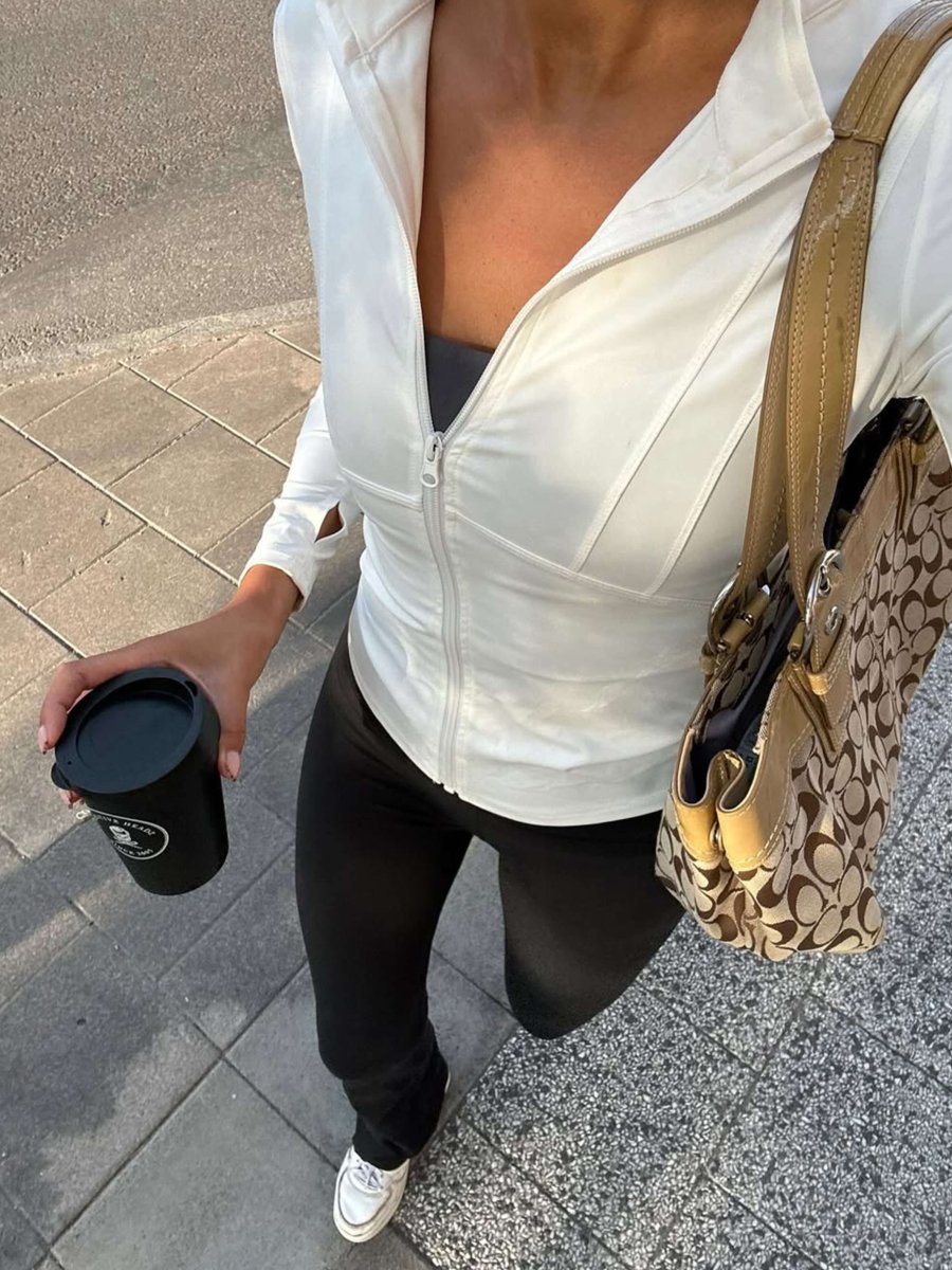Overhead view of a woman walking on a sidewalk in a white Kouvr Fashion Nola Sculpt Jacket and black leggings, holding a coffee cup and a designer bag.
