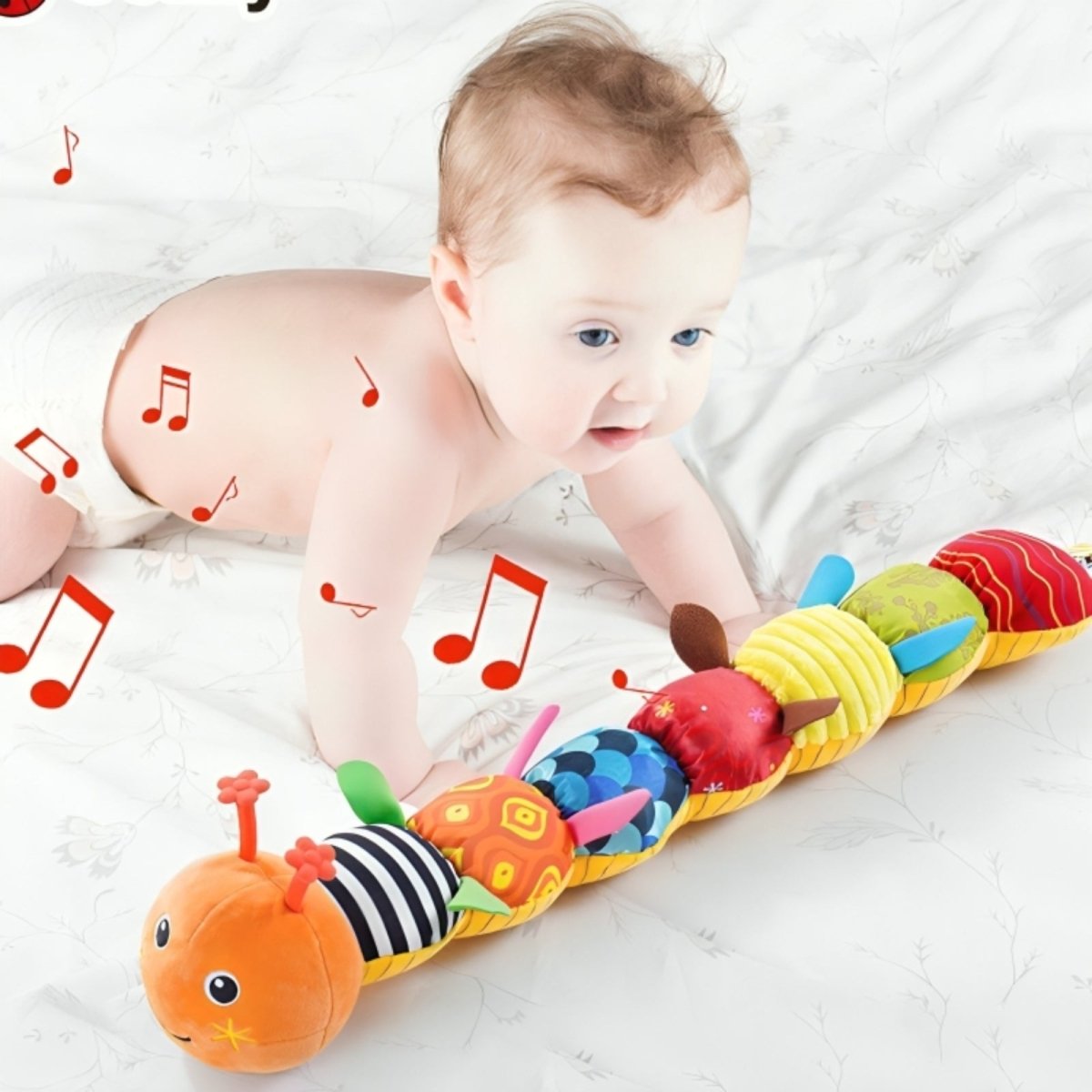Baby playing with a colorful caterpillar toy on a white surface.